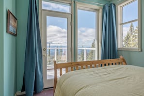 Relax in this serene bedroom with a large bed and a balcony offering a view of the surrounding landscape.