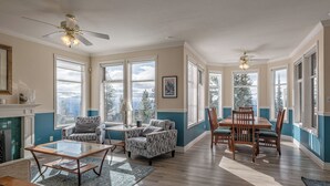 A spacious living room with a fireplace, large windows, and a dining area with a wooden table and chairs. - Large 5 bedroom, standalone home with private hot tub, BBQ and pet friendly too! (Silver Star Mountain)