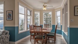 A dining room with a wooden table and chairs, large windows, and a ceiling fan. - Large 5 bedroom, standalone home with private hot tub, BBQ and pet friendly too! (Silver Star Mountain)