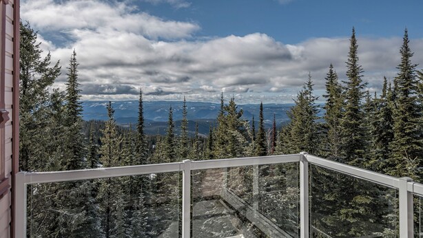 A balcony with a glass railing overlooking a forested mountain landscape. - Large 5 bedroom, standalone home with private hot tub, BBQ and pet friendly too! (Silver Star Mountain)