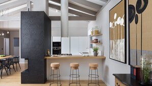 Een moderne keuken met een centraal eiland, barkrukken en een eethoek met een houten tafel en stoelen.