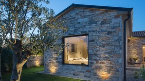 Een modern stenen gebouw met een groot glasraam dat een slaapkamer laat zien, met een bed en nachtkastje.