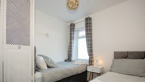 Une chambre à coucher avec un lit, une table de chevet avec une lampe, une armoire et une fenêtre avec des rideaux.