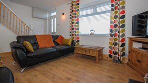 Un salon avec un canapé en cuir noir, une table basse en bois et un téléviseur posé sur un meuble en bois.