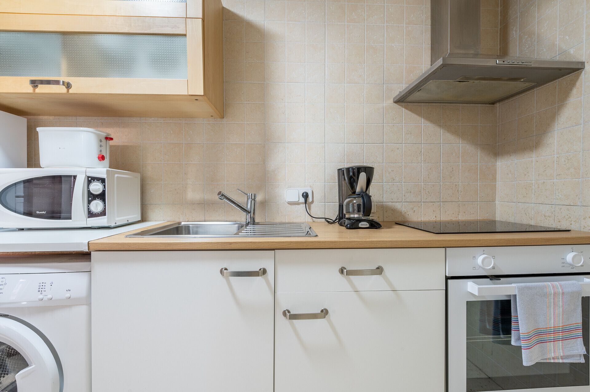 A kitchen with a microwave, coffee maker, sink, oven, and a washing machine.