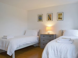 Un dormitorio con dos camas individuales, una mesita de noche con lámpara y tres cuadros en la pared.