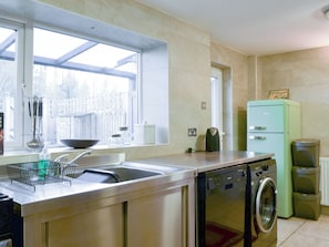 Una cocina con un lavabo, lavadora, refrigerador verde y ventana con vista a una cerca.