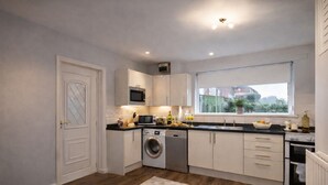 A compact kitchen with a washing machine, microwave, and a large window. - HC Property - Taylor Avenue (Durham)