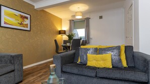 A living room with a grey sofa, yellow cushions, a framed picture on the wall, a lamp, and a window with curtains. - HC Property - Taylor Avenue (Durham)