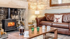 A cozy living room with a stone fireplace, leather sofa, and a coffee table. - 3 bedroom accommodation in Rothbury (Rothbury)