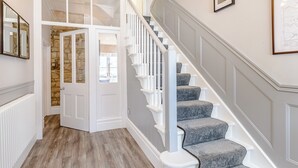 A staircase with white railings and grey carpeted steps, leading to a room with a stone wall and a white door. - 3 bedroom accommodation in Rothbury (Rothbury)
