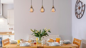 A dining area with a wooden table set for breakfast, a vase with flowers, and a wall clock. - 3 bedroom accommodation in Rothbury (Rothbury)