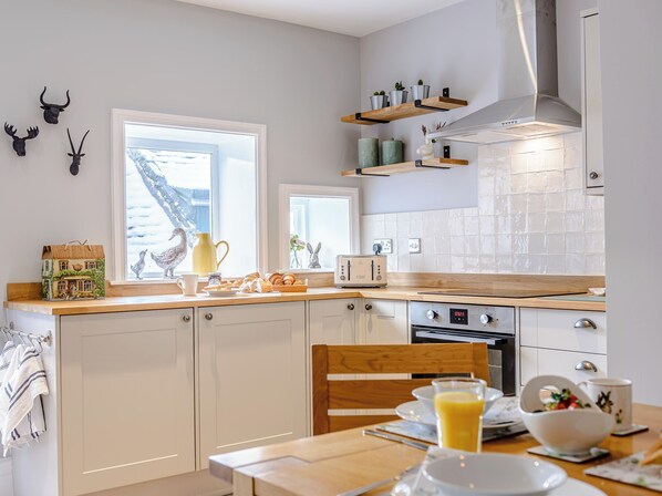 A modern kitchen with white cabinets, a wooden countertop, a built-in oven, and a window with a view of a snowy landscape.
