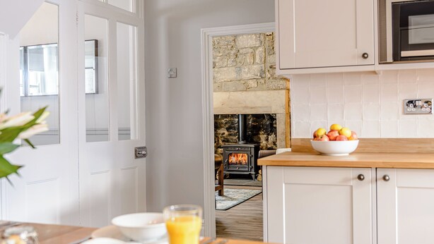 A modern kitchen with white cabinetry, a stone fireplace, and a bowl of fruit on the counter. - 3 bedroom accommodation in Rothbury (Rothbury)