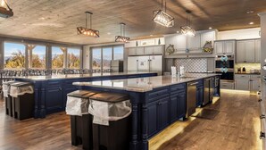 A spacious kitchen with a large island, wooden ceiling, and modern lighting fixtures. - Grand LeConte Lodge | 21BR Luxury Estate w/ Pool, Theater, Arcade, Sleeps 96 (Pigeon Forge)