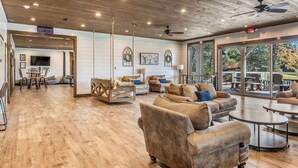 A spacious indoor area with wooden flooring, leather sofas, and a ceiling fan. - Grand LeConte Lodge | 21BR Luxury Estate w/ Pool, Theater, Arcade, Sleeps 96 (Pigeon Forge)