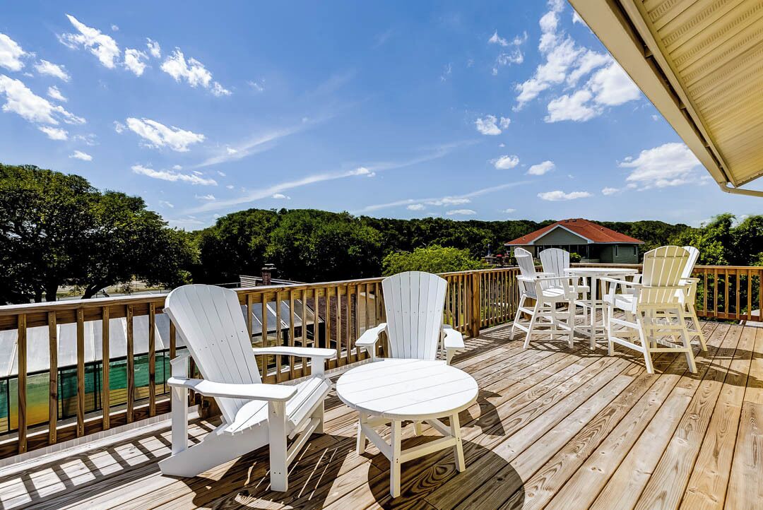A wooden deck with Adirondack chairs and a table, overlooking a body of water and trees.