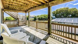 A covered outdoor deck with wooden railings, a white chair, and a view of solar panels and trees.