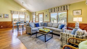 A spacious living room with a wooden floor, a sofa set, a dining table, and a ceiling fan.