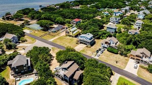 An aerial view of a residential area with houses, a swimming pool, and a road leading to the water.