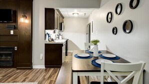 Una cocina moderna con armarios de madera oscura, horno empotrado y comedor con mesa de madera y sillas blancas.