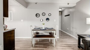 Un comedor con una mesa blanca, un banco de madera oscura y sillas blancas. Hay espejos circulares montados en la pared y un jarrón blanco con flores sobre la mesa.