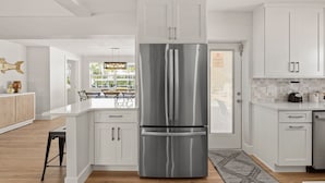 Een moderne keuken met witte kasten, een roestvrijstalen koelkast en een eetgedeelte met natuurlijk licht.