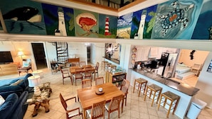 Un vaste espace de vie comprenant un coin repas avec table et chaises, une cuisine équipée d’appareils modernes et un escalier menant à l’étage supérieur.