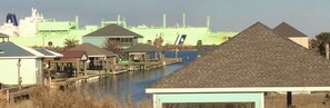 A waterfront property with a dock, a small building with a sloped roof, and a large industrial facility in the background.
