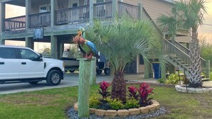 A two-story building with a balcony, a parking area, and a landscaped garden with a palm tree and colorful plants. - 10% Discount- Hackberry Hideaway II Water View On Lake Calcasieu (Hackberry)