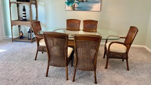 A dining area with a glass table surrounded by wicker chairs, a hanging light fixture, and a painting of a sailboat on the wall.