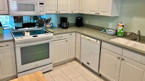 A modern kitchen with white cabinets, a microwave, stove, dishwasher, and a coffee maker.