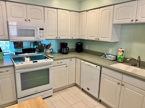 Una cocina moderna con armarios blancos, microondas, estufa, lavavajillas y cafetera.