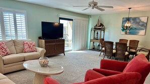 A living room with a beige sofa, red armchairs, a coffee table, and a dining area with wicker chairs.