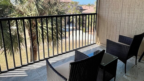 A balcony with a table and chairs, a ceiling fan, and a view of palm trees and houses.