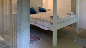 A four-poster bed with a quilt and pillows, a white brick wall, and a hanging light fixture.