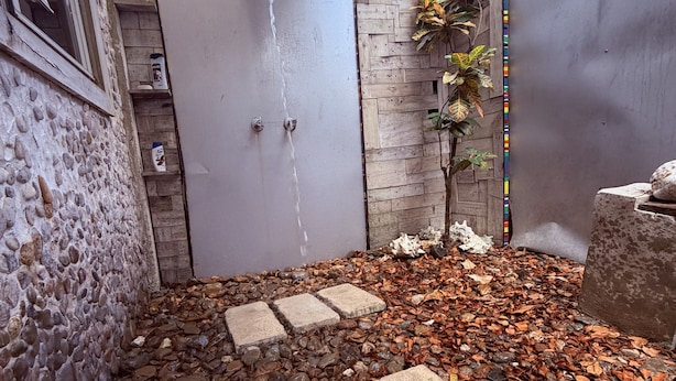 A stone wall, a concrete door with a water spout, a small plant, and a gravel path.