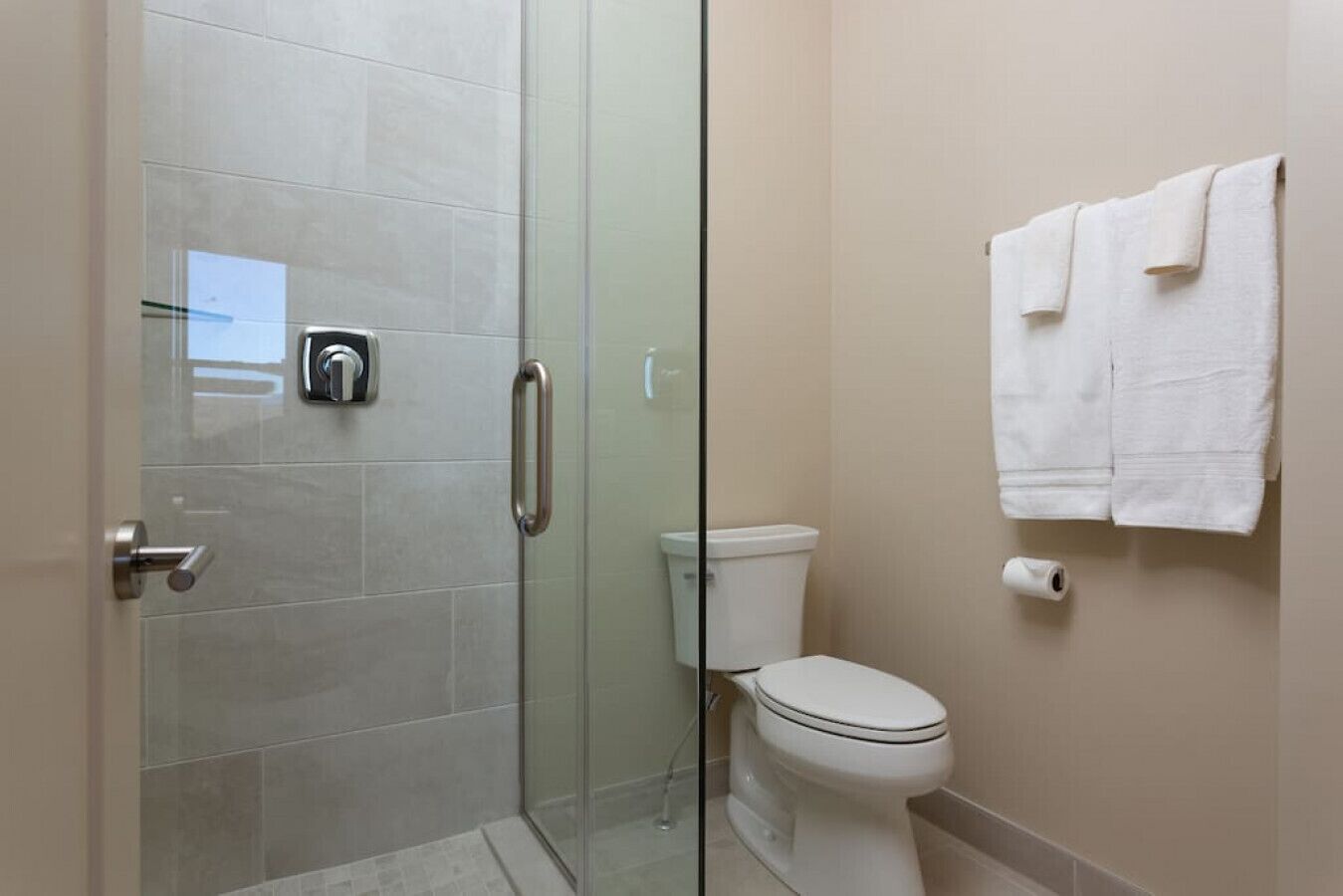 Un baño con cabina de ducha de vidrio, inodoro y un perchero con toallas.