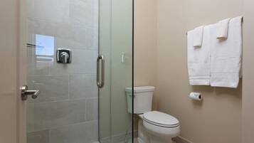 Un baño con cabina de ducha de vidrio, inodoro y un perchero con toallas.