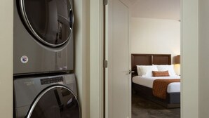 A hotel room with a bed, a nightstand, and a wall-mounted washer and dryer.