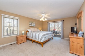 A bedroom with a bed, a nightstand, a dresser, a ceiling fan, and a large window.