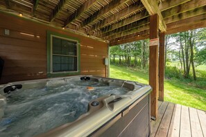 A hot tub under a wooden pergola with a view of a grassy area and trees.