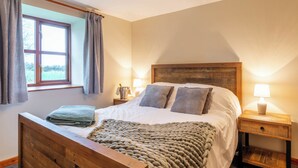 Une chambre à coucher avec une tête de lit en bois, un grand lit recouvert de draps blancs, un plaid en tissu tissé, deux lampes de chevet et une fenêtre avec des rideaux.