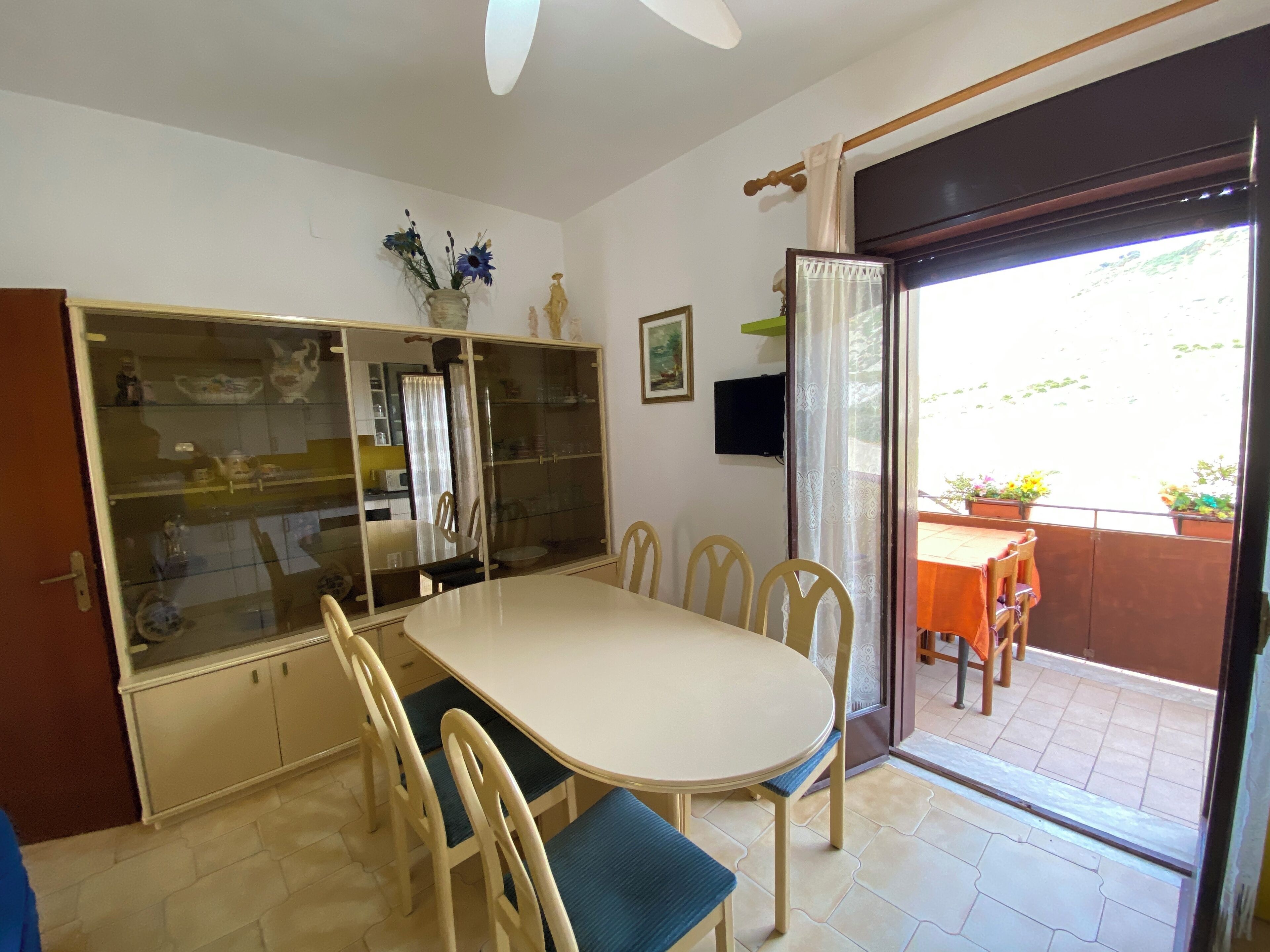 A dining area with a round table, six chairs, a glass display cabinet, and a sliding glass door leading to an outdoor patio.