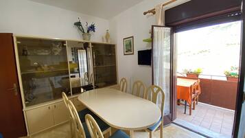 Un coin repas comprenant une table ronde, six chaises, un meuble vitré et une porte-fenêtre coulissante donnant sur une terrasse extérieure.