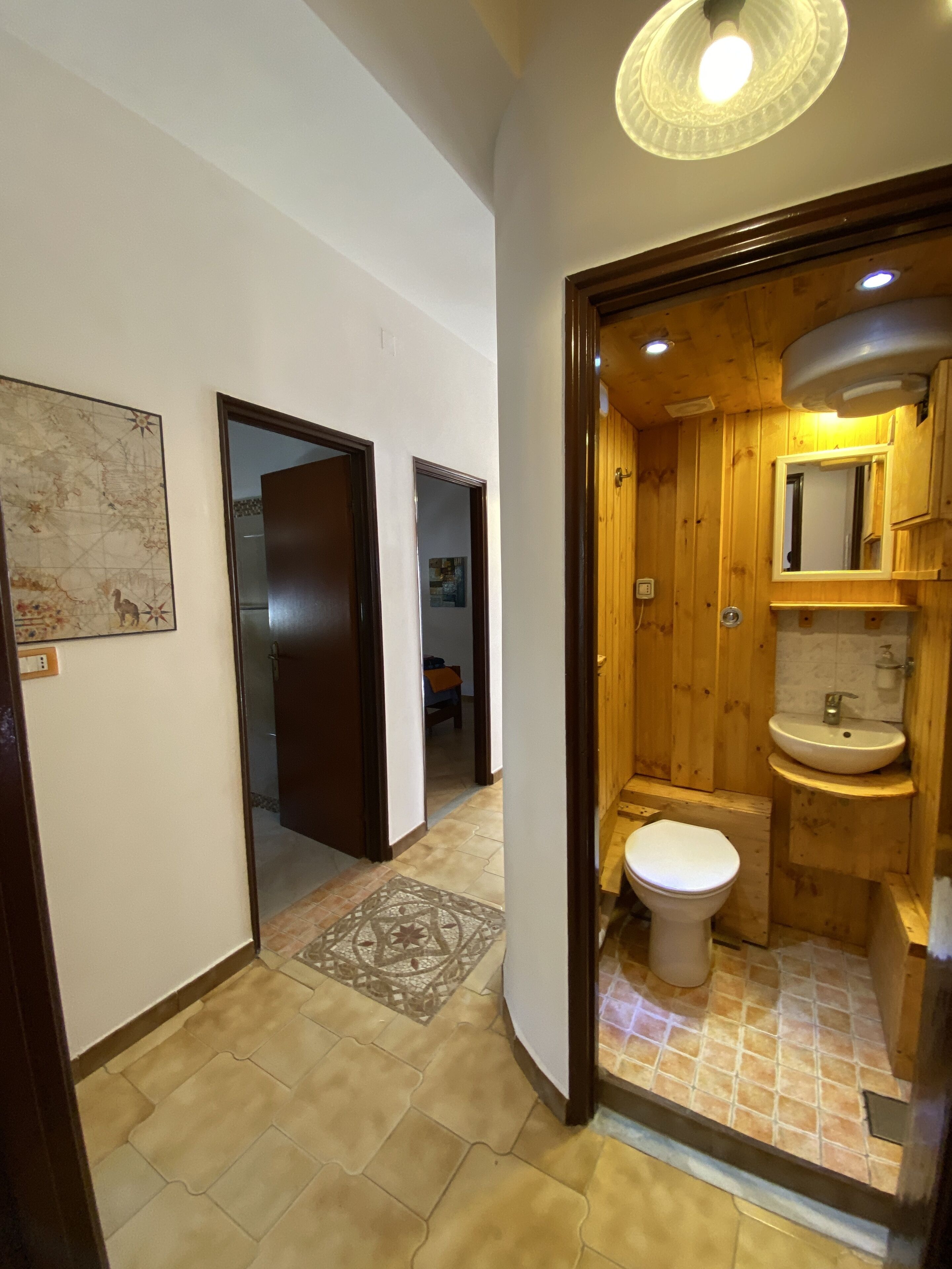 Un pasillo que conduce a un baño de madera con inodoro, lavamanos y espejo.