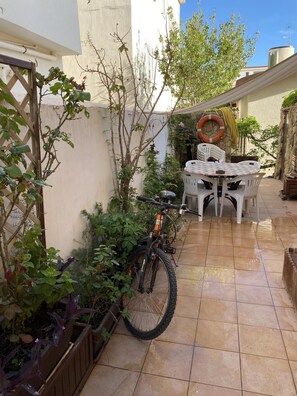 Uma área de pátio com uma bicicleta, uma mesa com cadeiras e diversas plantas.