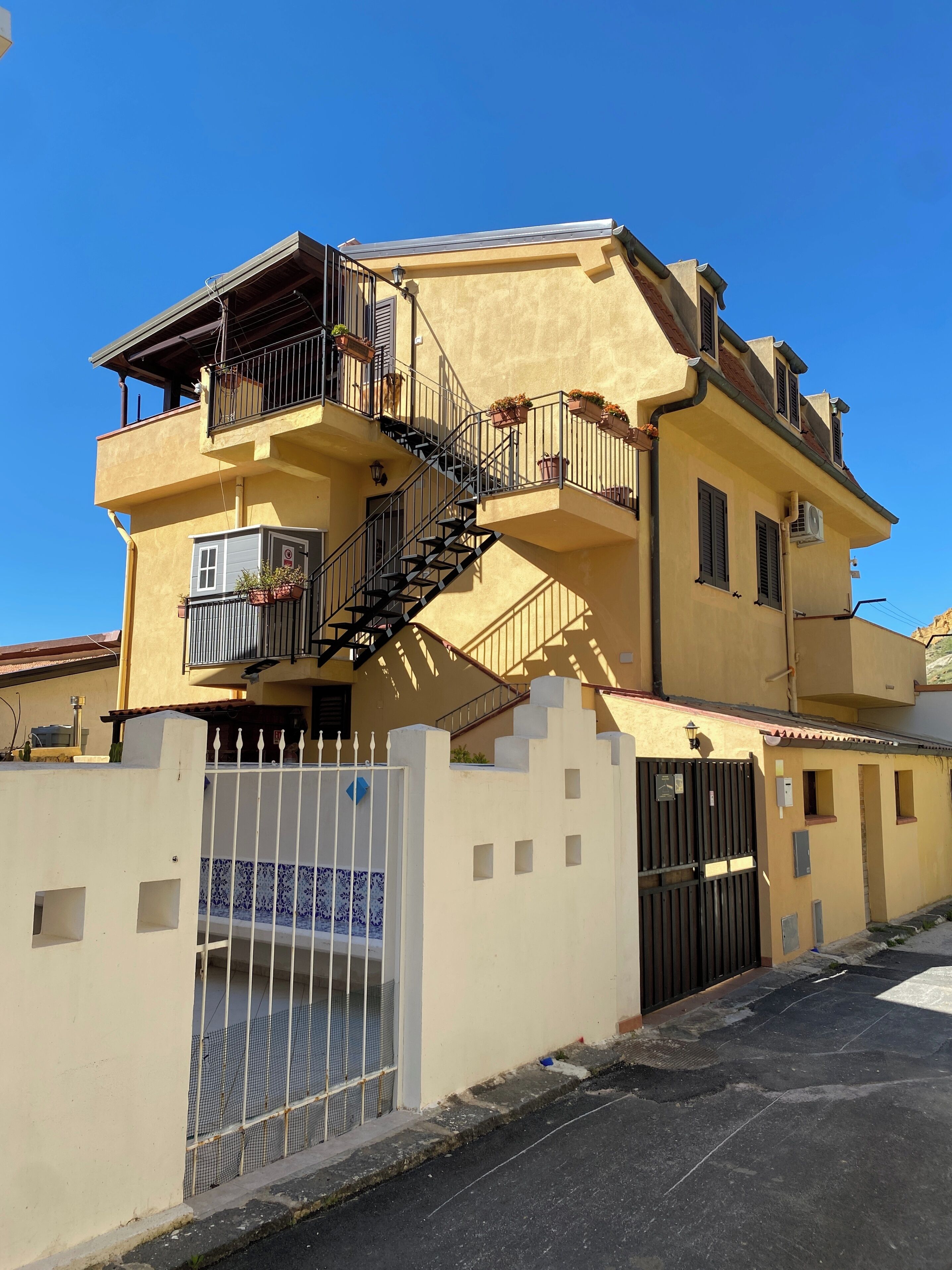 Un edifici de diversos pisos amb un balcó, una escala i una entrada tancada per una reixa.