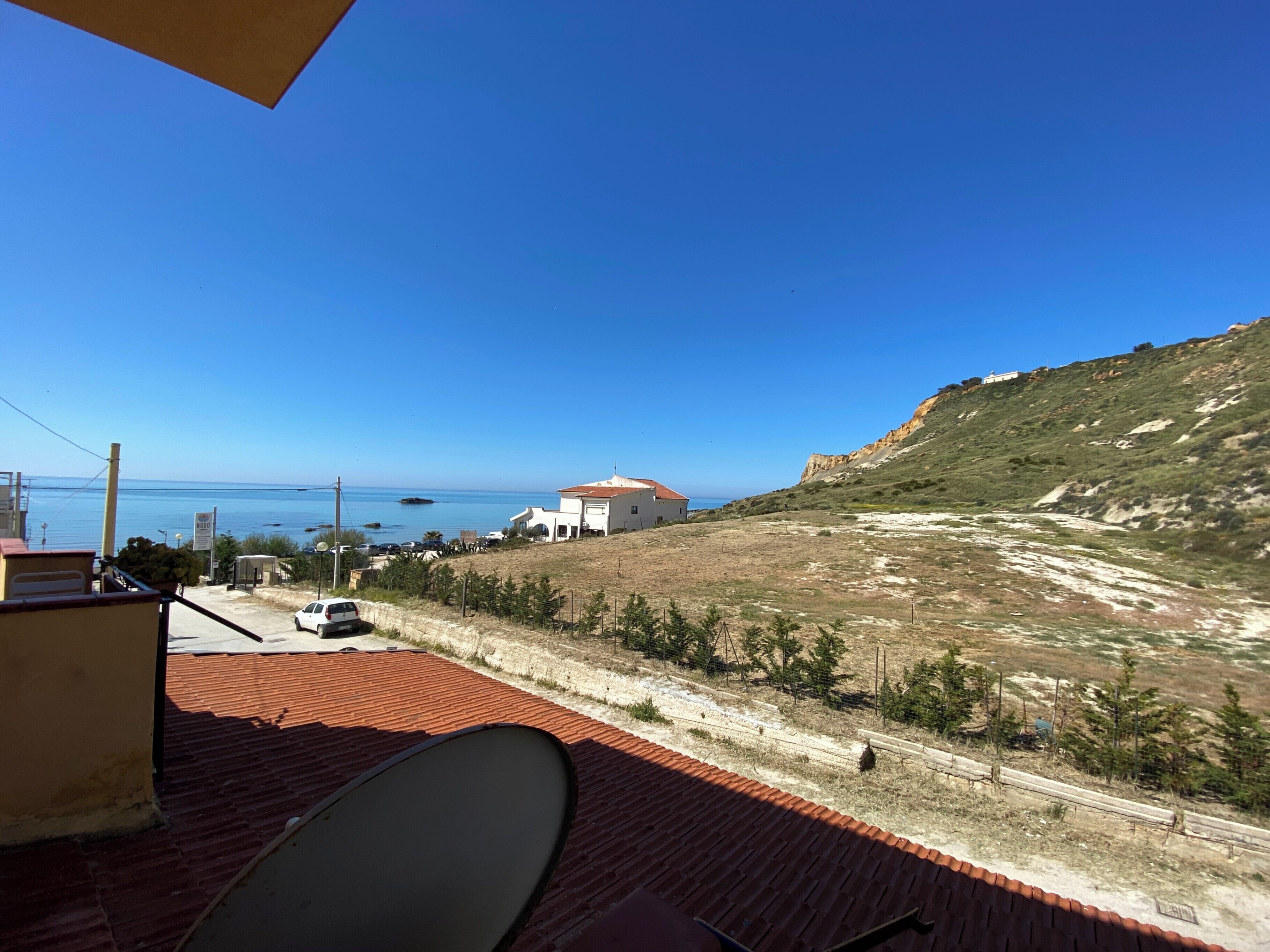 Um terraço com vista para o mar, um edifício branco e uma paisagem acidentada.