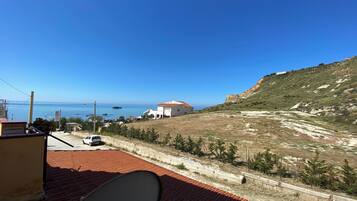 Um terraço com vista para o mar, um edifício branco e uma paisagem acidentada.